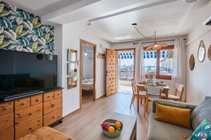 A living room with a TV, wooden furniture, a dining area with a table and chairs, and a balcony with a view. - Naufragos Beach 1 (Torrevieja)