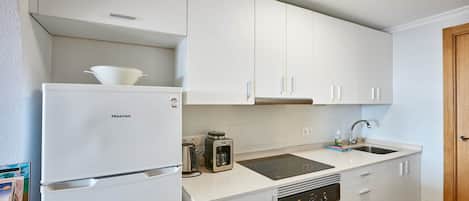 Eine kleine Küche mit weißen Schränken, einem Backofen, einer Spüle und einem Hisense-Kühlschrank.