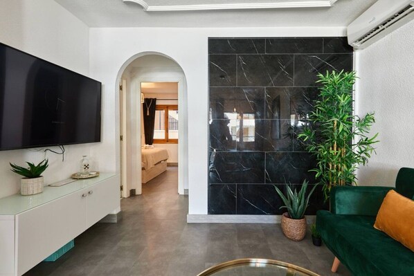 Un salon moderne avec un téléviseur à écran plat, un canapé vert, une grande plante en pot et un mur en marbre.