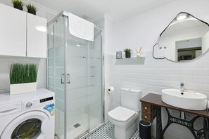 A modern bathroom with a glass-enclosed shower, a white toilet, and a sink with a mirror above it.