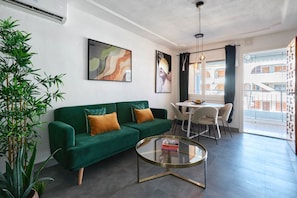 Una sala de estar moderna con un sofá verde, una mesa de centro de vidrio y un comedor con una mesa y sillas blancas.