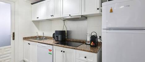 Cozinha com armários brancos, uma cafeteira preta, geladeira e micro-ondas.