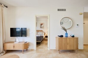Une chambre d’hôtel équipée d’une télévision, d’une table de chevet, d’un lit avec une tête de lit, d’un miroir fixé au mur et d’une petite armoire.
