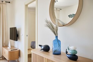 Une salle de bain moderne avec un meuble-lavabo en bois, un miroir rond et des éléments décoratifs, notamment un vase contenant des plantes séchées et une sculpture.