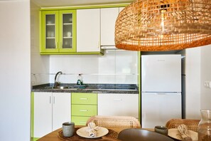 Une cuisine avec des meubles de couleur verte, un réfrigérateur blanc et un luminaire suspendu en fibres tressées.