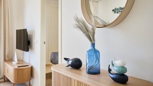 Ein modernes Badezimmer mit einem Holzbadezimmer-Möbel, einer blauen Vase mit getrockneten Pflanzen und einem runden Spiegel an der Wand.