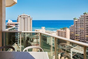 Un balcon offrant une vue sur l’océan et sur le paysage urbain, notamment les immeubles de grande hauteur et un parking.