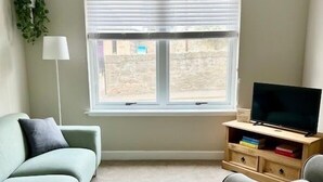 Ein Wohnzimmer mit einer Couch, einem Sessel, einem Fernsehschrank und einem Fenster mit Jalousien.