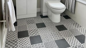 Ein Badezimmer mit einem weißen Waschbecken, einer Toilette und einer Badewanne. Über dem Waschbecken befindet sich ein Fenster und an der Wand ein Spiegel.
