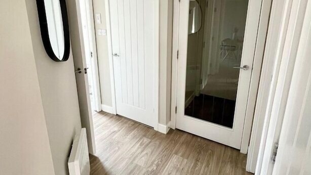 Ein Flur mit Holzboden, weißen Türen und einem Spiegel an der Wand.