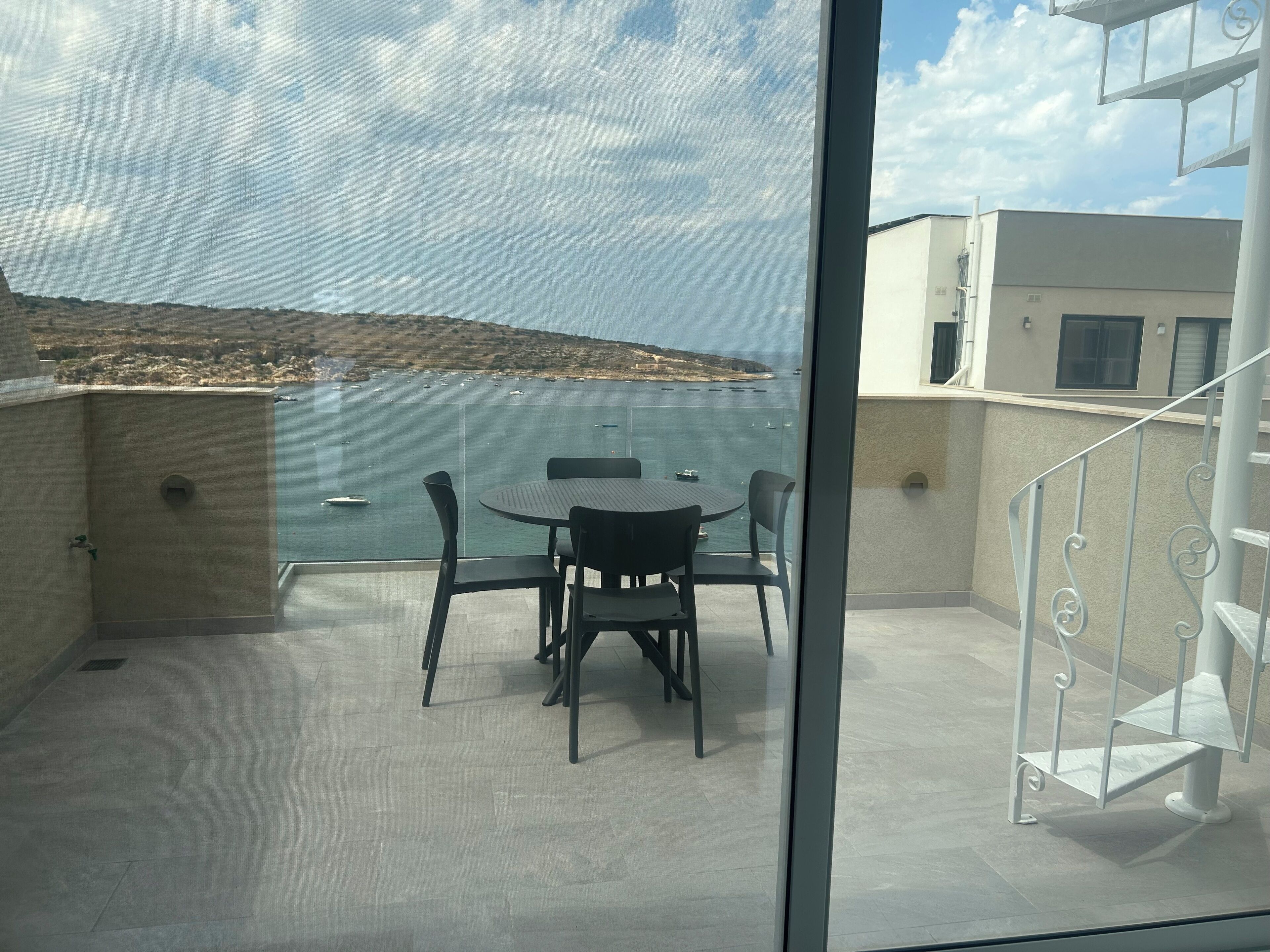 Varanda com mesa e cadeiras redondas, com vista para um corpo d'água e uma terra distante.