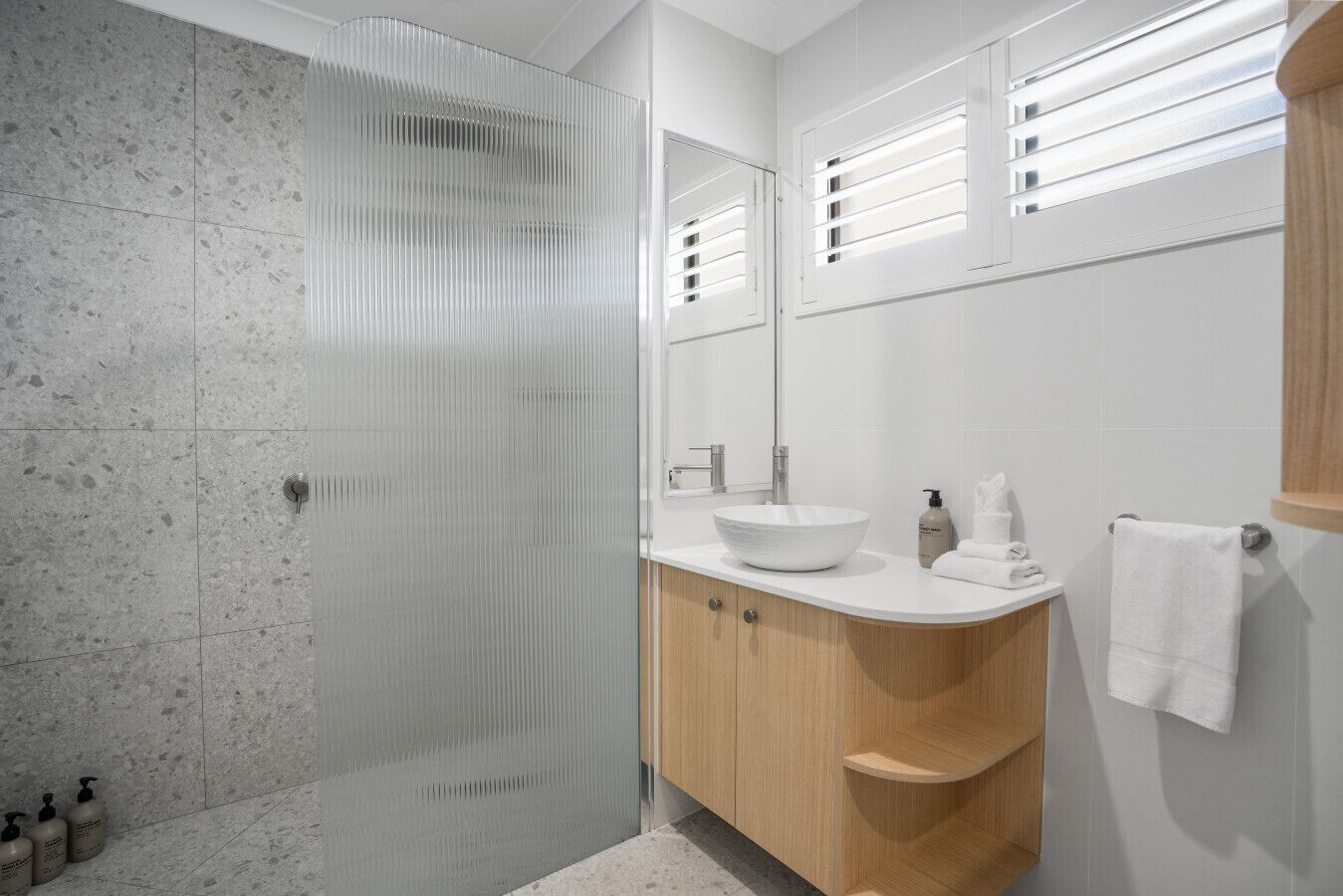 A modern bathroom with a glass shower enclosure, a white sink with a wooden vanity, and a large mirror.