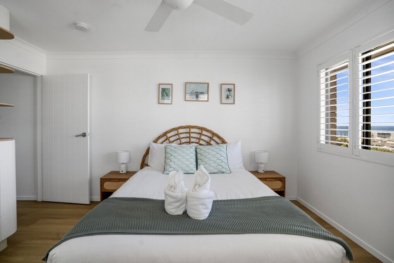 Een keurig opgemaakt slaapkamer met een bed, twee nachtkastjes, een deur en een raam met jaloezieën.