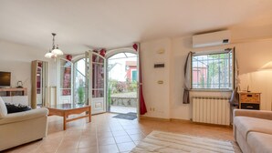 A spacious living room with a sofa, a coffee table, and a TV. There is a large window with a view of the outside, and a radiator on the wall. - 1 bedroom gorgeous apartment in Masso (Masso)