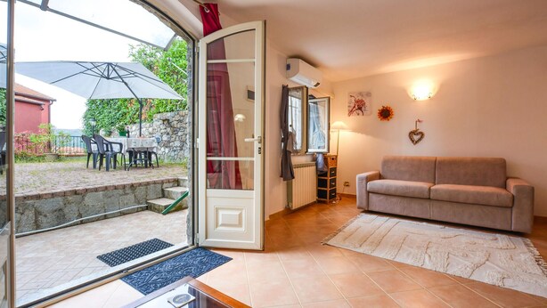 A cozy living room with a beige sofa, a dining area with a table and chairs, and a view of a red building through a glass door. - 1 bedroom gorgeous apartment in Masso (Masso)