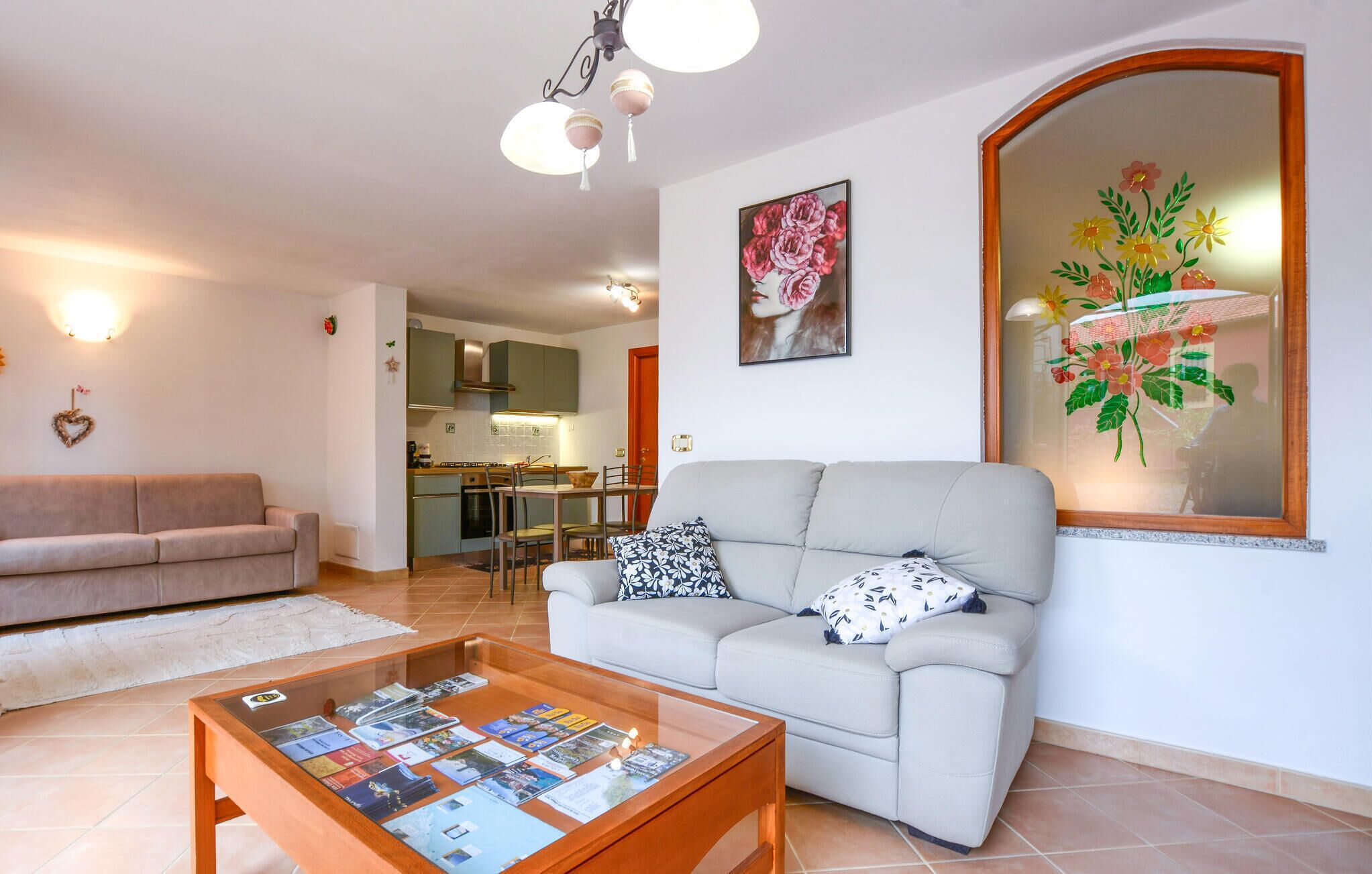 Una sala de estar con un sofá, una mesa de centro con revistas, una cocina al fondo y una gran obra de arte floral en la pared.
