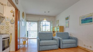 Olohuoneessa on sohva, pieni pöytä ja kaappi. Siellä on ikkuna, josta avautuu näkymä puita kohti, ja ovi, joka johtaa toiseen huoneeseen.