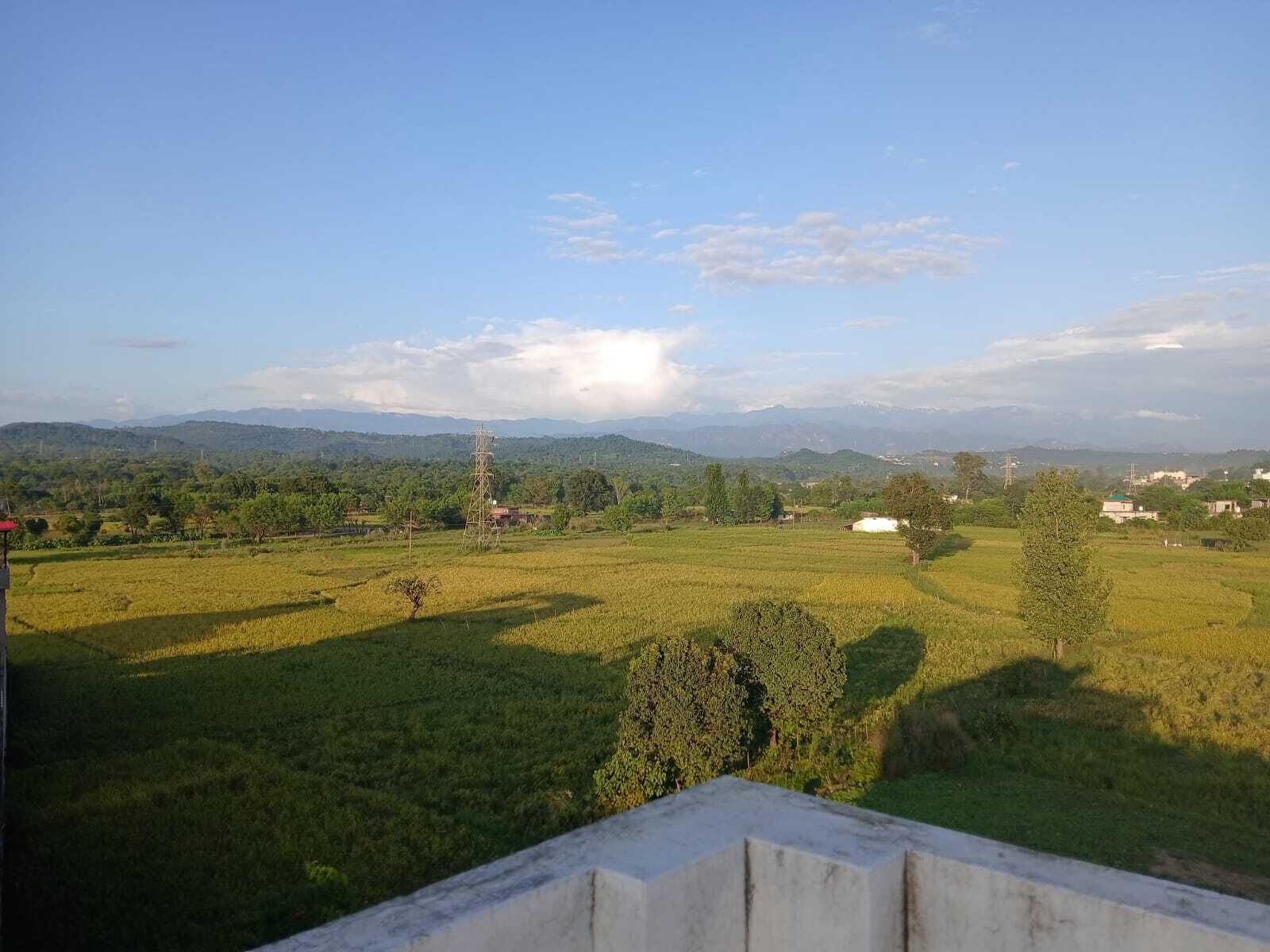 Paisaje rural con campos, árboles y montañas a lo lejos.
