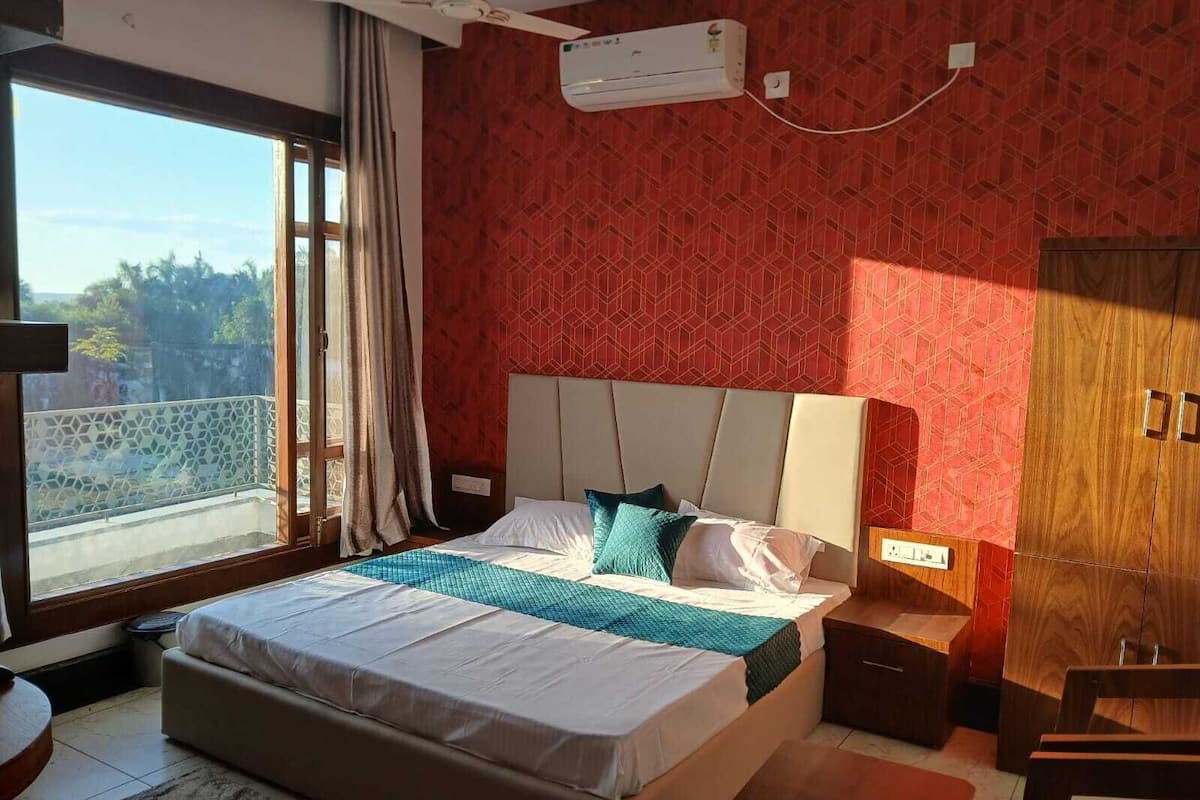 A hotel room with a large bed, a nightstand, a wardrobe, and a window with a view of greenery.