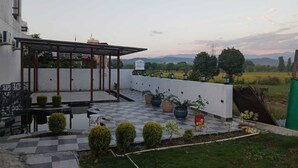 Terraço no telhado com pérgola, plantas em vasos e vista para o campo.