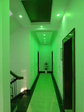 Un pasillo con techo e paredes iluminadas en verde, una planta en maceta y una escalera a la izquierda.