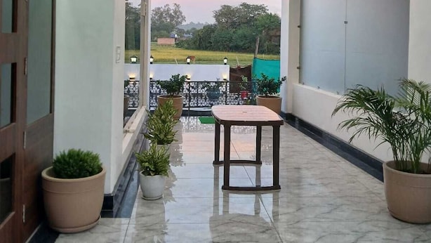 Amplo espaço interno com piso de mármore, mesa de madeira e plantas em vasos.