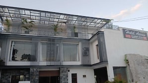 Hotel moderno com fachada de vidro, varanda com plantas e placa indicando instalações como piscina e restaurante.