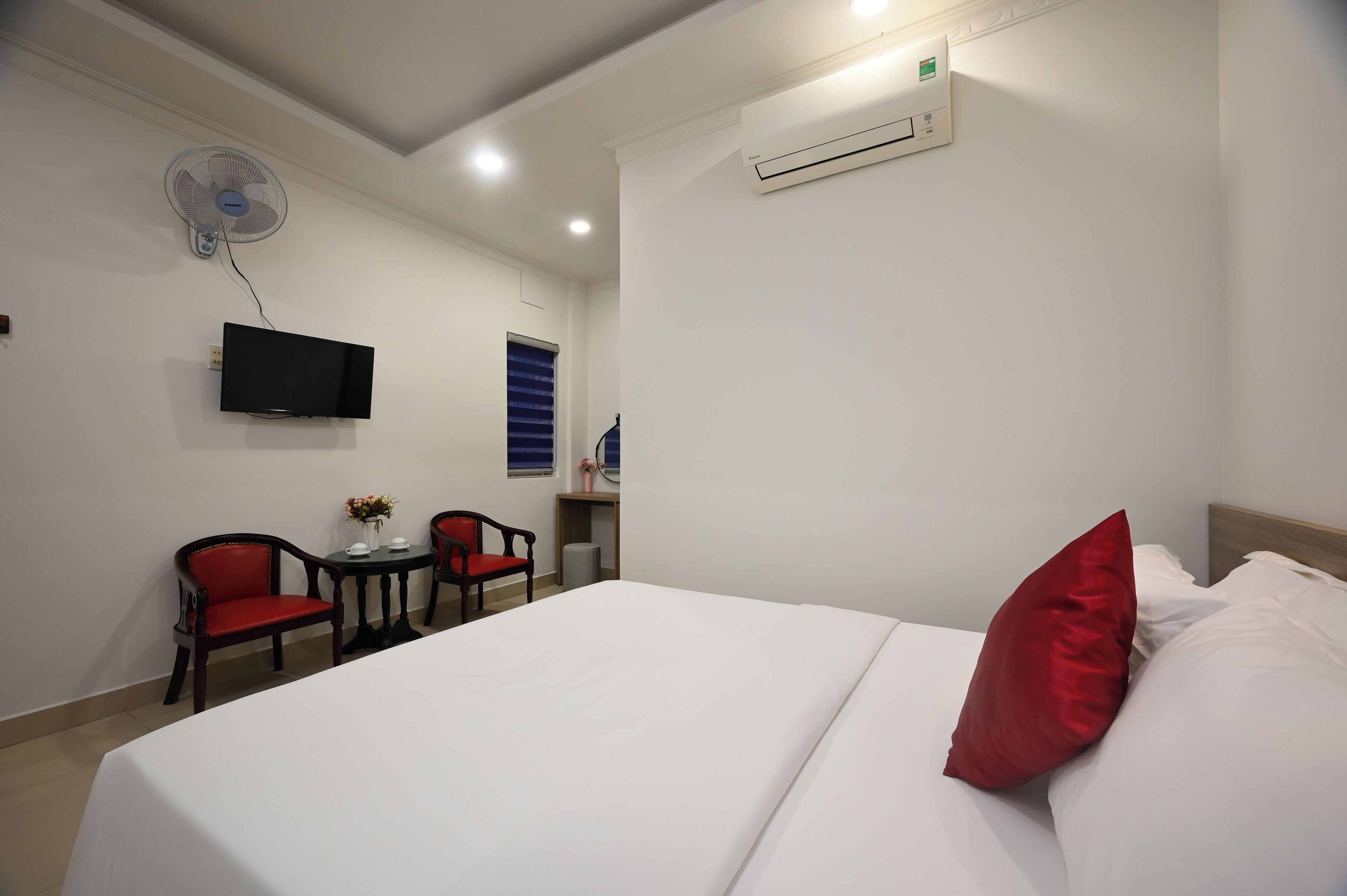 A hotel room with a bed, a TV mounted on the wall, a ceiling fan, and an air conditioning unit.