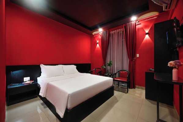 A modern hotel room with a large bed, a desk, a chair, and a TV.