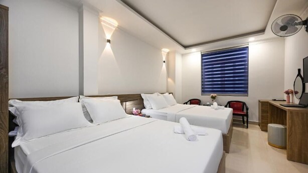 A hotel room with two beds, a desk, a chair, a standing fan, and a window with blinds. - Hotel Trung Mai-Tân Bình (Ho Chi Minh City)