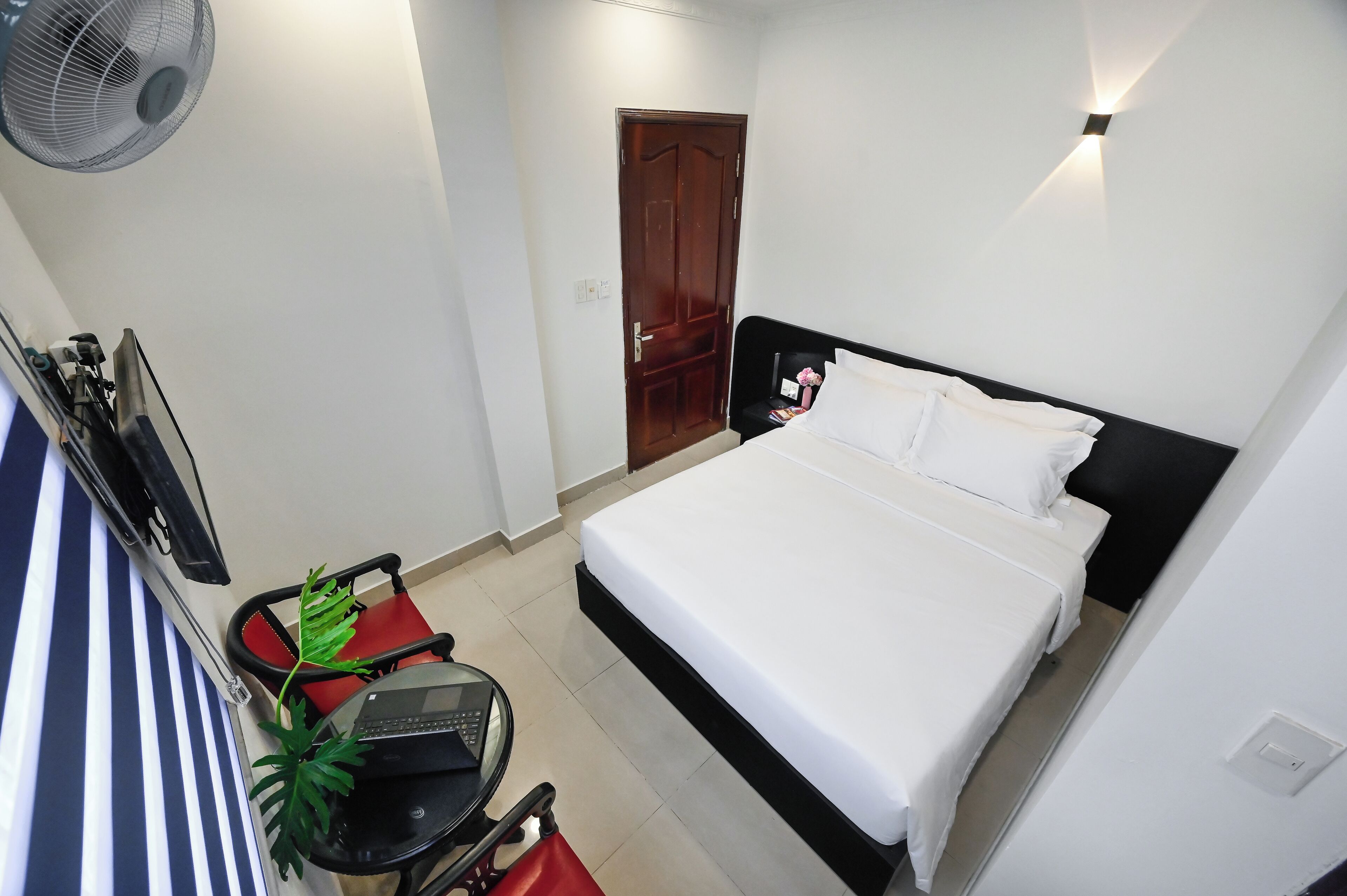 Una habitación de hotel con cama, escritorio, silla, ventilador y puerta.