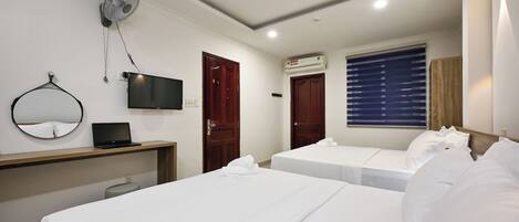 A hotel room with two beds, a desk with a laptop, a TV, a wall-mounted fan, and an air conditioning unit.