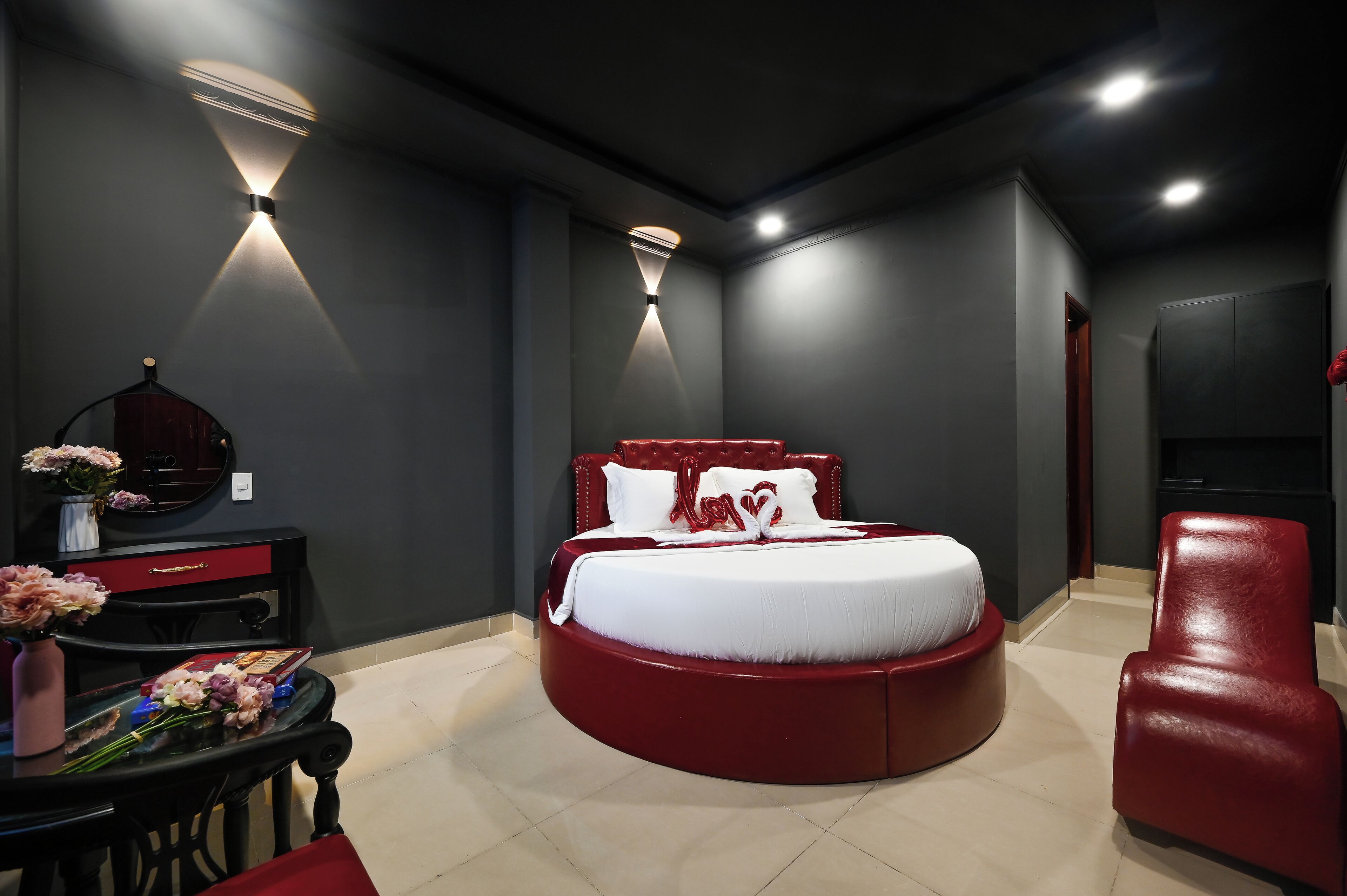 A modern bedroom with a round bed, a red chair, and a desk with flowers.