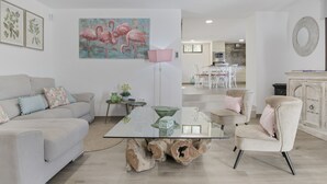 Ett modernt vardagsrum med ett soffbord i glas, en soffa, en fåtölj och en tavla med flamingos på väggen.