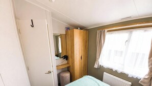 Una habitación con una cama, un armario de madera, un radiador, una ventana con cortinas y una puerta con manija.
