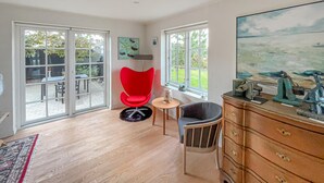 A spacious room with a large sliding glass door leading to an outdoor patio, a red chair, a wooden dresser, and a painting on the wall. - Beautiful home in Esbjerg V with WiFi (Esbjerg V)