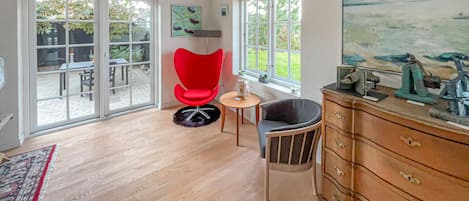 A spacious room with a large sliding glass door leading to an outdoor patio, a red chair, a wooden dresser, and a painting on the wall.