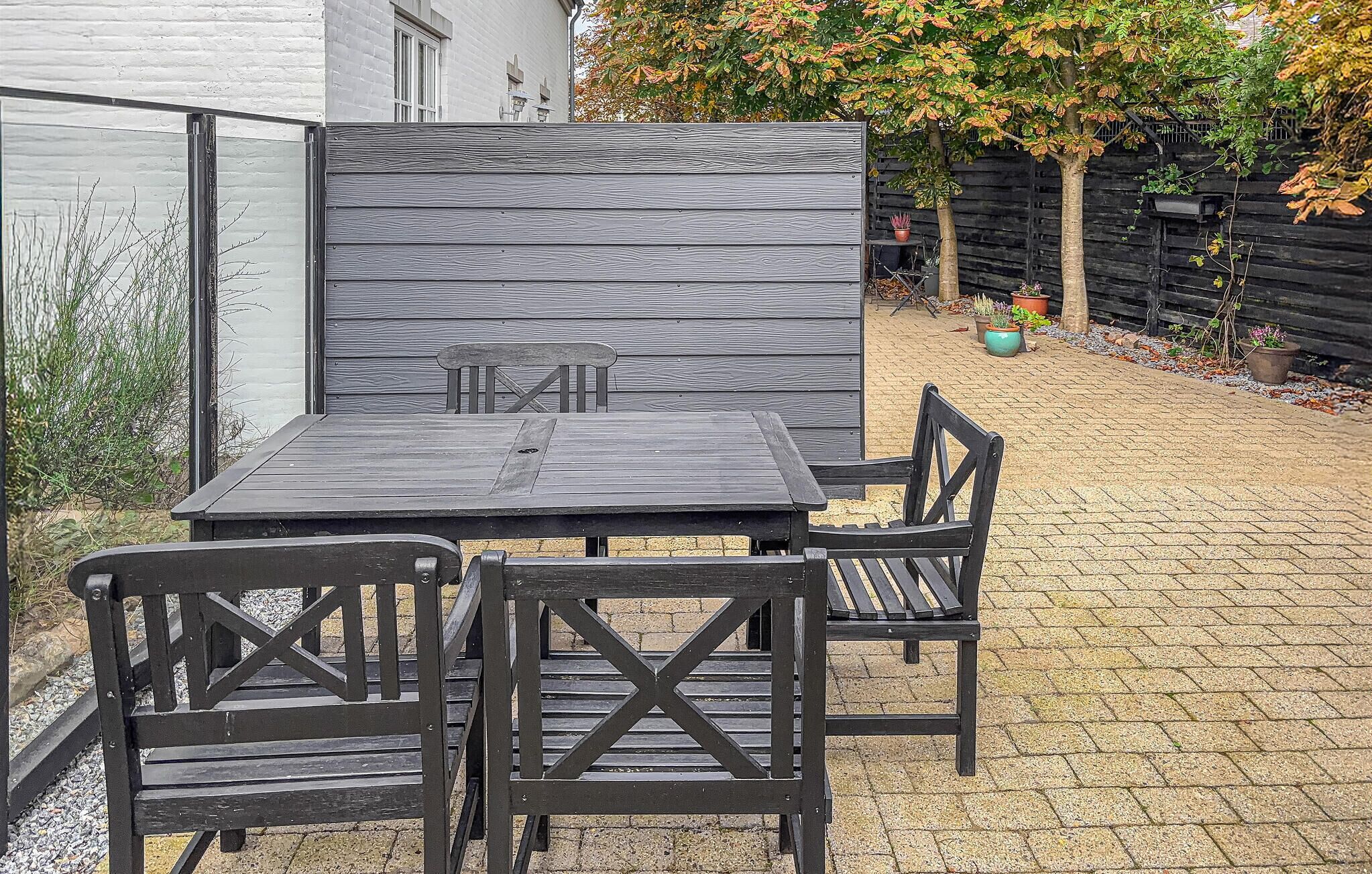 Eine Terrass mit Holztable und -stühlen, umgeben von einem Pflasterboden und einem Holzzaun.