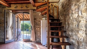 A rustic interior with a wooden spiral staircase, stone walls, and a glass door leading to an outdoor area. - La Casina Cottage by Geco Vacation Rentals (Bucine)