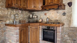A kitchen with wooden cabinets, a brick wall, a stove, and a sink. - La Casina Cottage by Geco Vacation Rentals (Bucine)