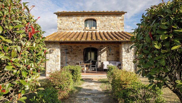 A stone building with a tiled roof, a central doorway, and a small window above it. There is a table and chairs outside the building. - La Casina Cottage by Geco Vacation Rentals (Bucine)