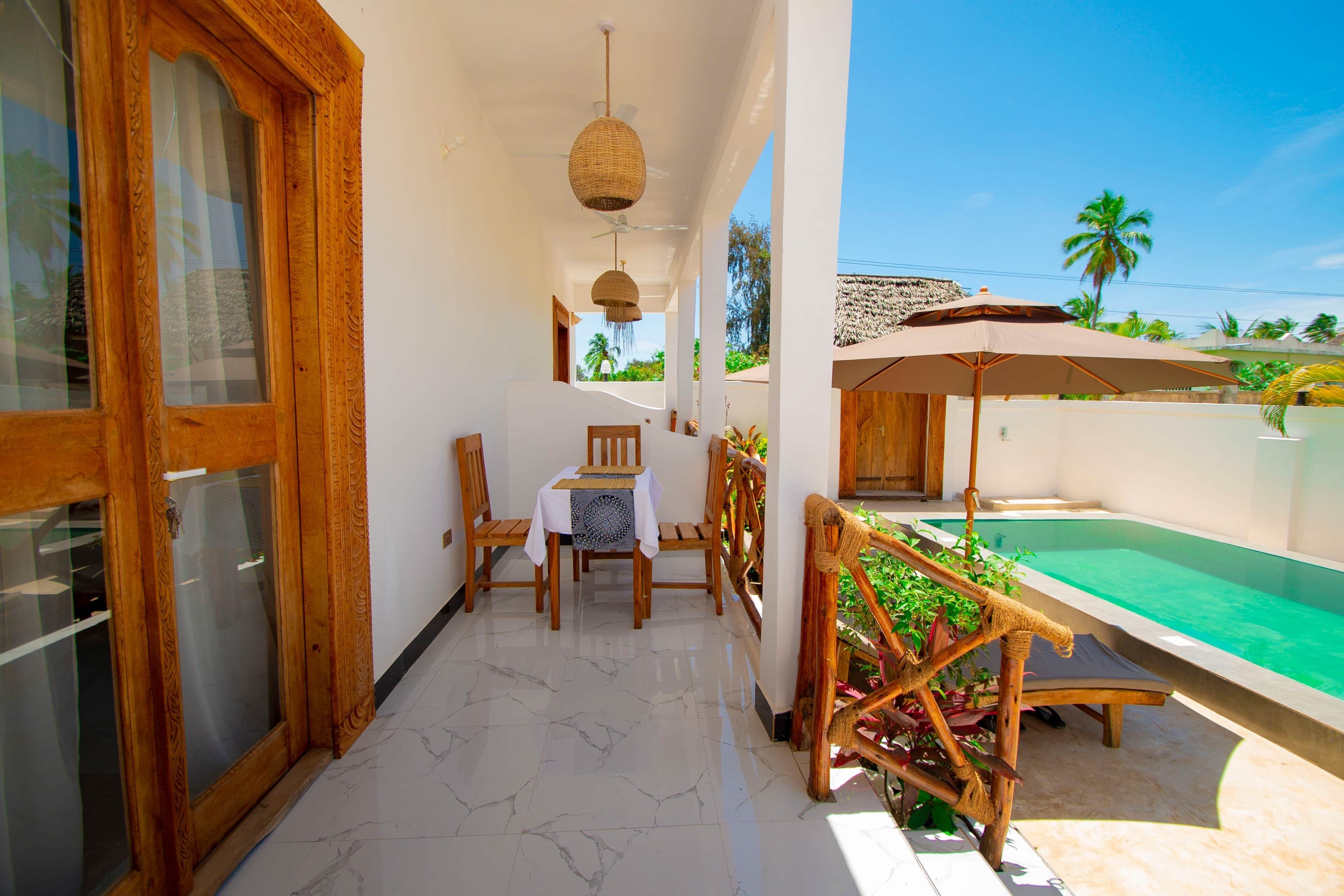 A balcony with a table and chairs, a pool, and a view of palm trees.