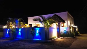 A modern building with a white facade, a thatched roof, and a blue-lit water feature in the foreground.