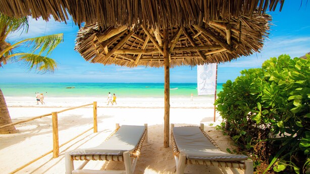 A beach with two lounge chairs under a thatched roof, a sandy path, and a clear view of the ocean. - Zanzibar Marea suites A (Kiwengwa)