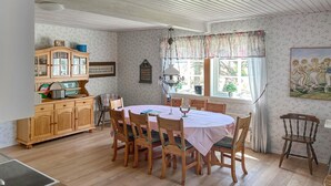 A dining room with a round table, wooden chairs, and a checkered tablecloth. There is a wooden cabinet with glass doors and a hanging light fixture above the table.