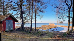 A cabin with a red exterior and a blue door, surrounded by trees and a view of a lake.