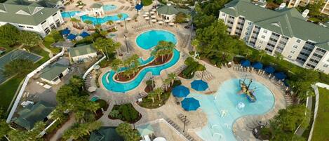 An aerial view of a resort with multiple swimming pools, sun loungers, and a boat in one of the pools.