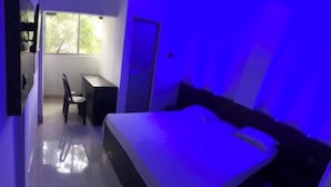 A bedroom with a bed, a desk, and a chair. There is a window providing natural light. - HOTEL SIDHU  (Jamshedpur)