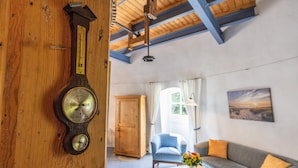 A room with a wooden wall clock, a sofa, a table with a vase, and a door in the background. - Holiday Home 'Windmill Betty by the North Sea' with Private Terrace, Private Garden and Wi-Fi (Cuxhaven)