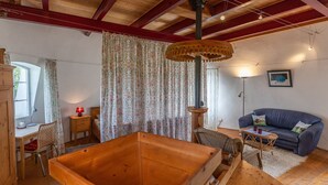 A wooden interior with a large wooden box, a blue sofa, and a wicker chair. - Holiday Home 'Windmill Betty by the North Sea' with Private Terrace, Private Garden and Wi-Fi (Cuxhaven)